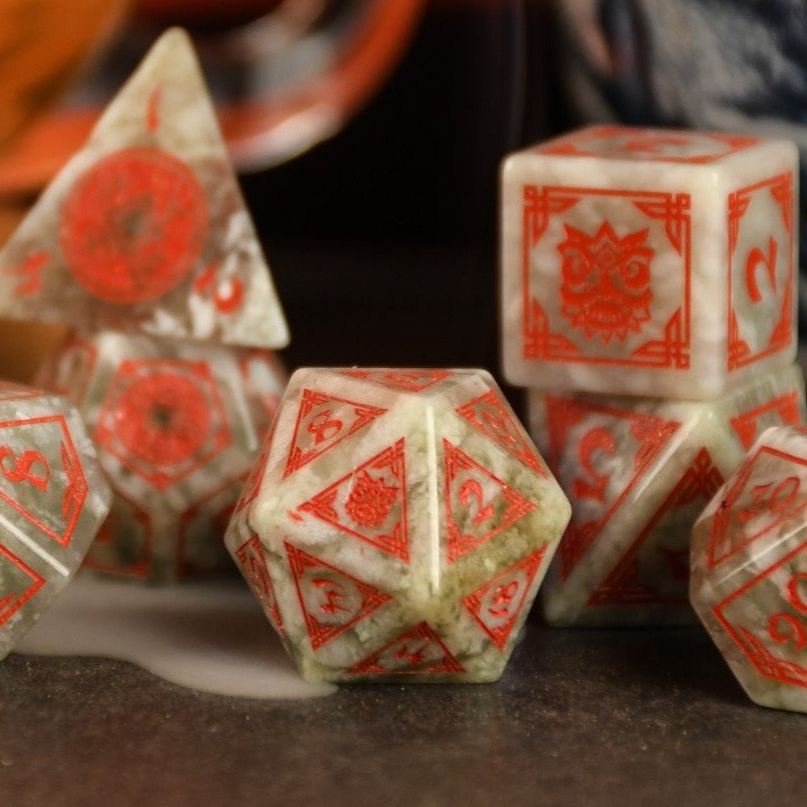 A set of hand-carved, Chinese Jade Stone Dice traditional Chinese patterns, displayed on a table with a cup and saucer in the background.