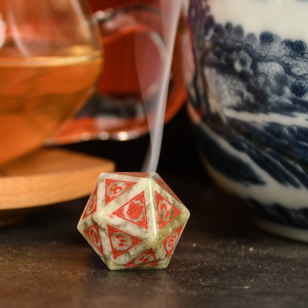 A set of hand-carved, Chinese Jade Stone Dice traditional Chinese patterns, displayed on a table with a cup and saucer in the background.