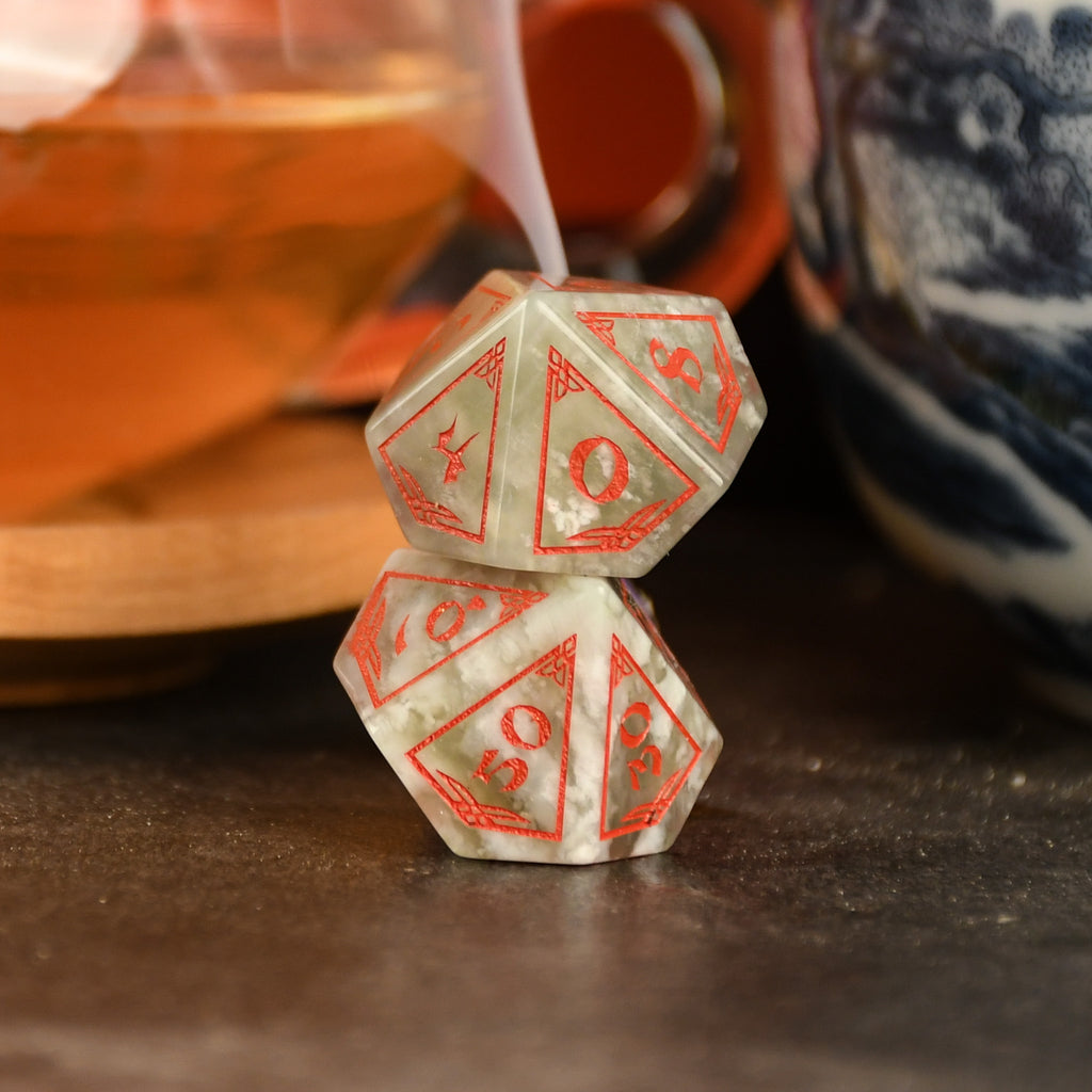 A set of hand-carved, Chinese Jade Stone Dice traditional Chinese patterns, displayed on a table with a cup and saucer in the background.