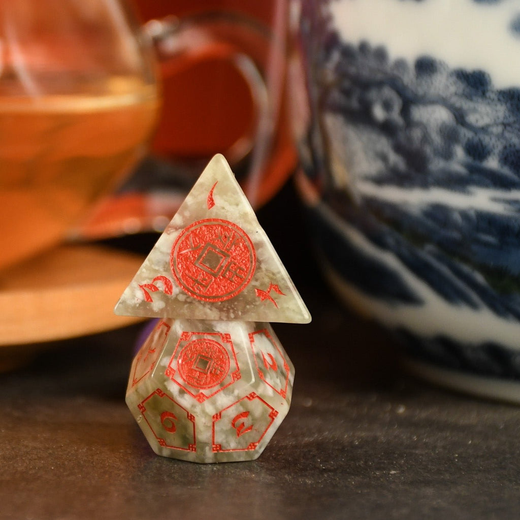 A set of hand-carved, Chinese Jade Stone Dice traditional Chinese patterns, displayed on a table with a cup and saucer in the background.
