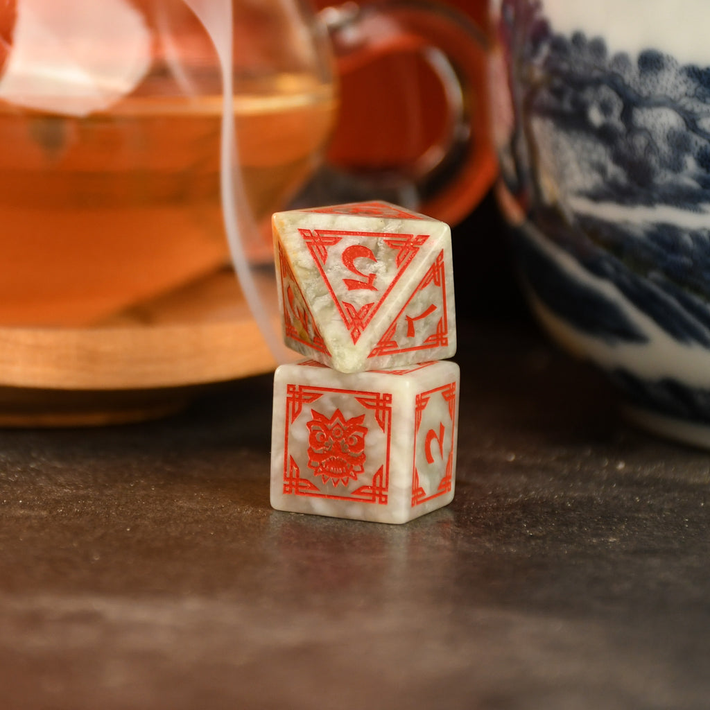 A set of hand-carved, Chinese Jade Stone Dice traditional Chinese patterns, displayed on a table with a cup and saucer in the background.
