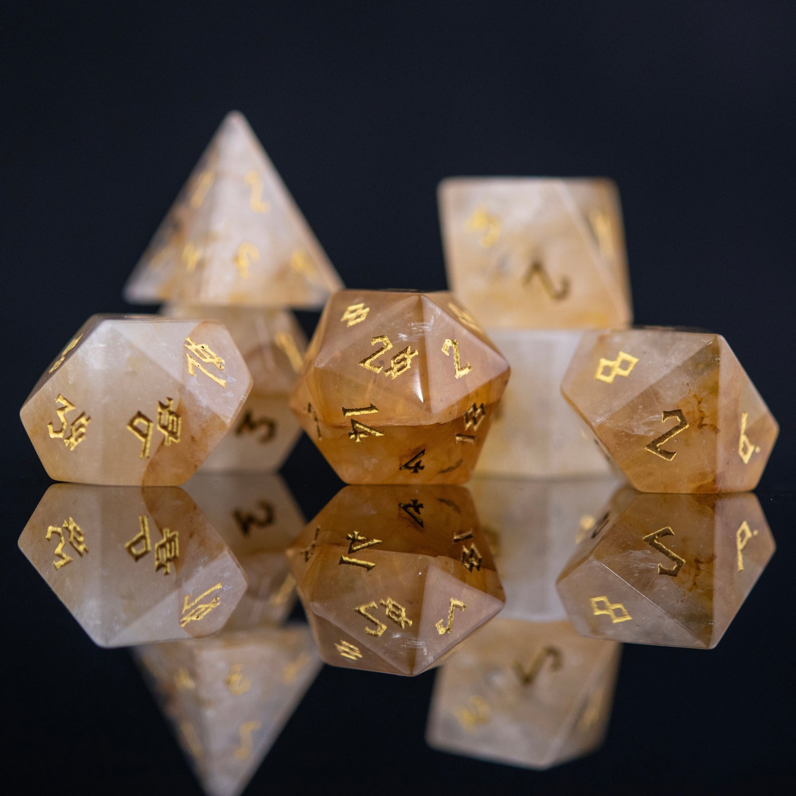 A collection of hand-carved and polished citrine stone dice with golden numbering, reflecting on a black surface.