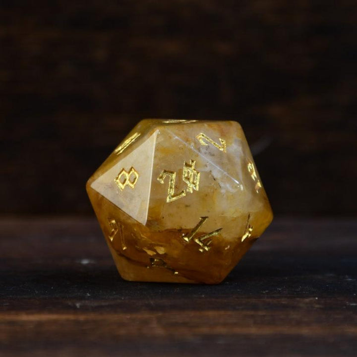 hand-carved and polished citrine stone die with golden numbering, reflecting on a black surface.