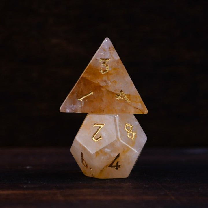 hand-carved and polished citrine stone die with golden numbering, reflecting on a black surface.