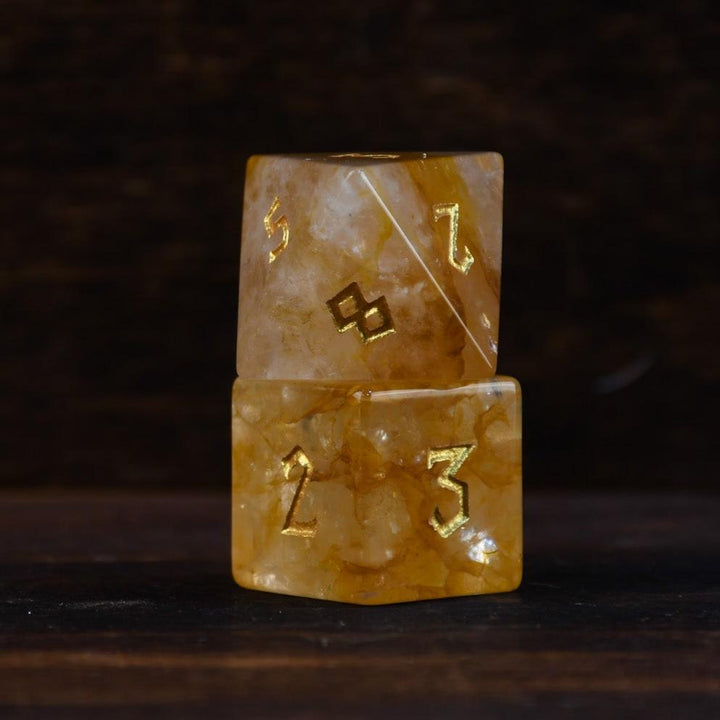hand-carved and polished citrine stone die with golden numbering, reflecting on a black surface.