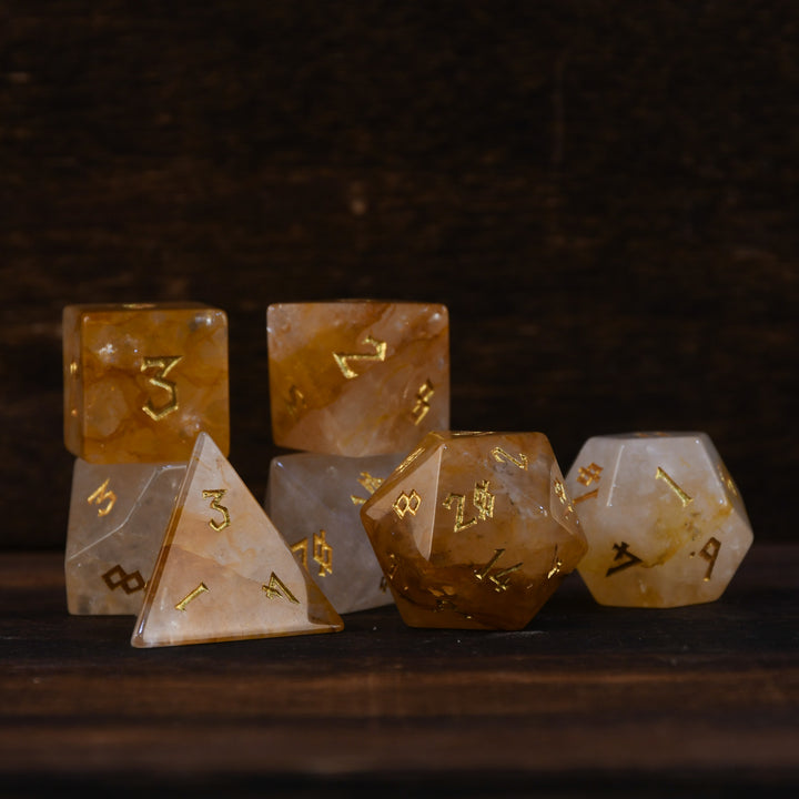 A collection of hand-carved and polished citrine stone dice with golden numbering, reflecting on a wooden surface.