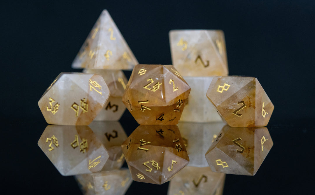A collection of hand-carved and polished citrine stone dice with golden numbering, reflecting on a black surface.