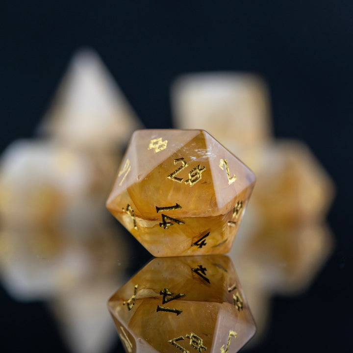 A collection of hand-carved and polished citrine stone dice with golden numbering, reflecting on a black surface.