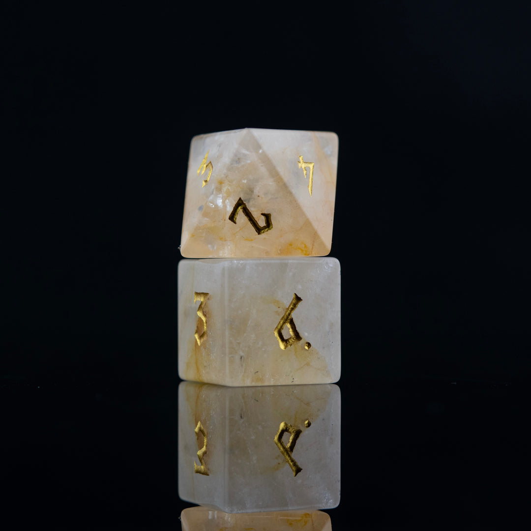 A collection of hand-carved and polished citrine stone dice with golden numbering, reflecting on a black surface.