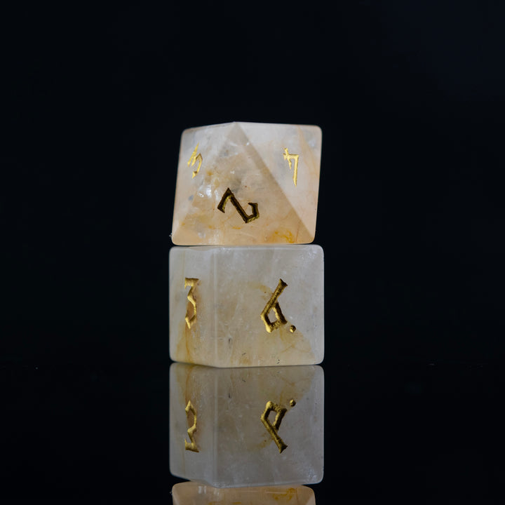 A collection of hand-carved and polished citrine stone dice with golden numbering, reflecting on a black surface.