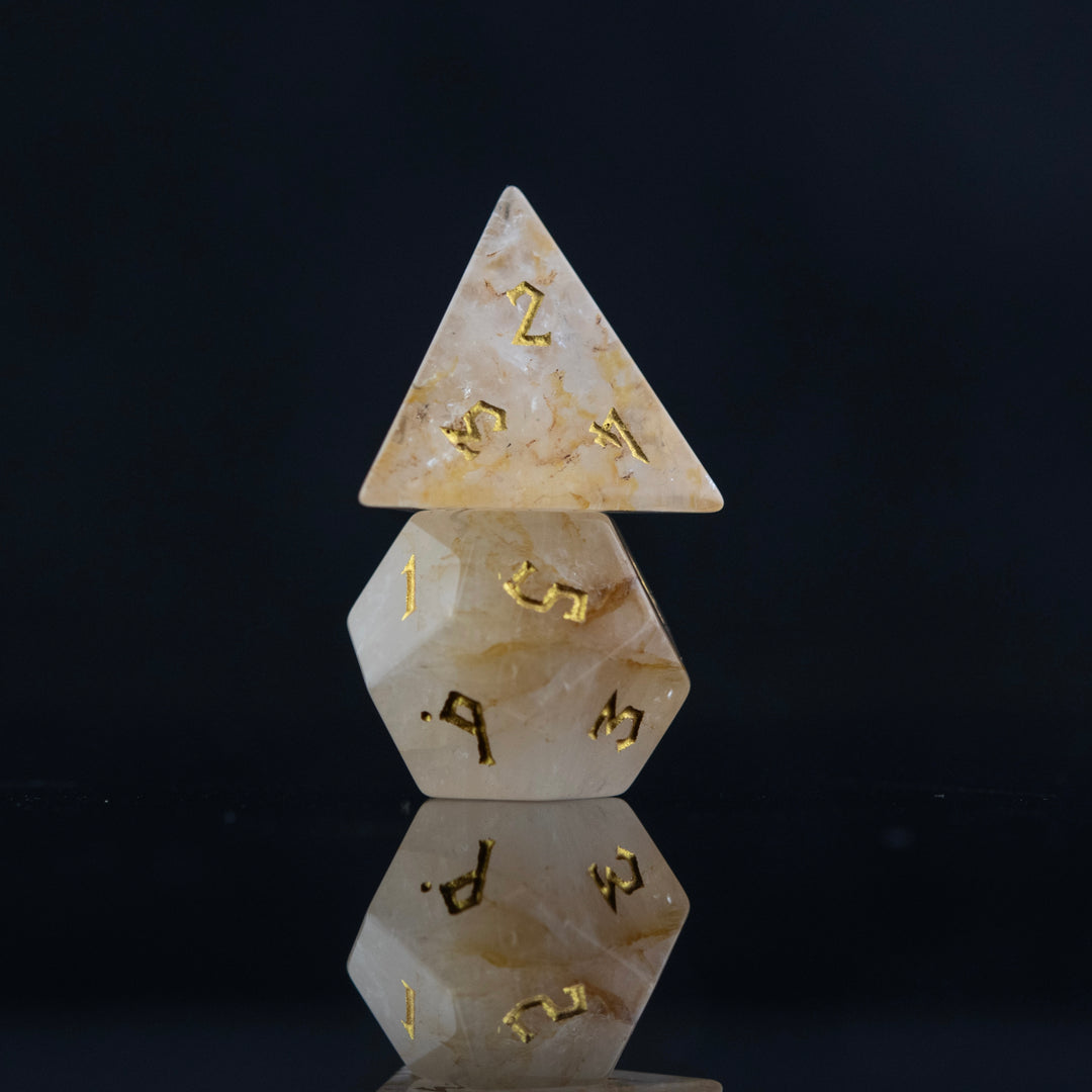 A collection of hand-carved and polished citrine stone dice with golden numbering, reflecting on a black surface.