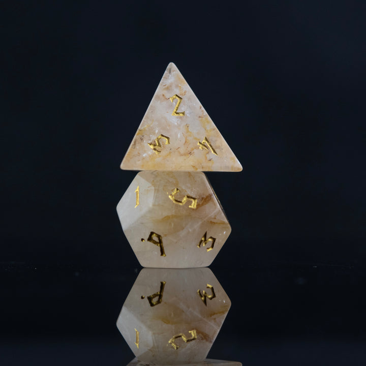 A collection of hand-carved and polished citrine stone dice with golden numbering, reflecting on a black surface.