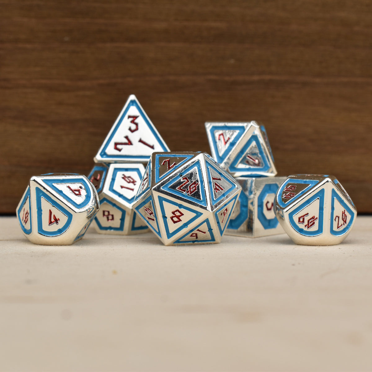 A set of silver polyhedral metal dnd dice with blue borders on each face and red numbering