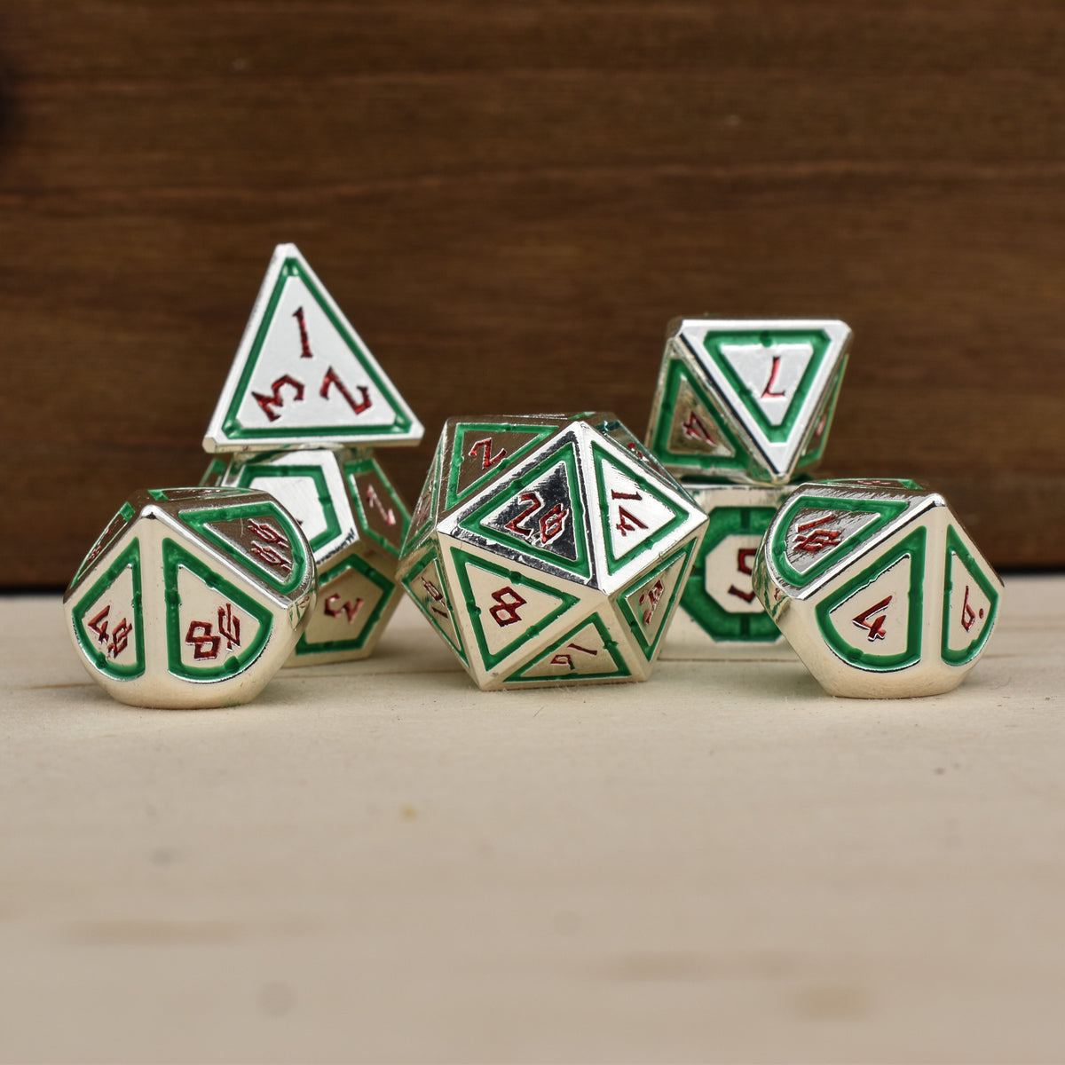 A set of silver polyhedral metal dnd dice with green borders on each face and red numbering