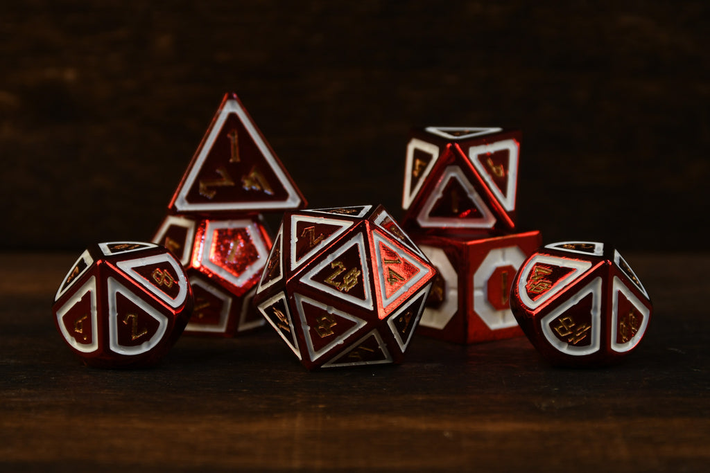 A set of red and white metal ttrpg dice with engraved numbers on a wooden surface.