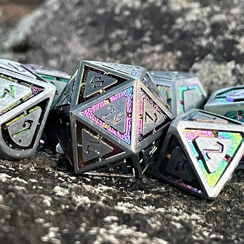 A set of silver metal dnd dice with iridescent properties, including engraved numbers, displayed on a rocky surface.