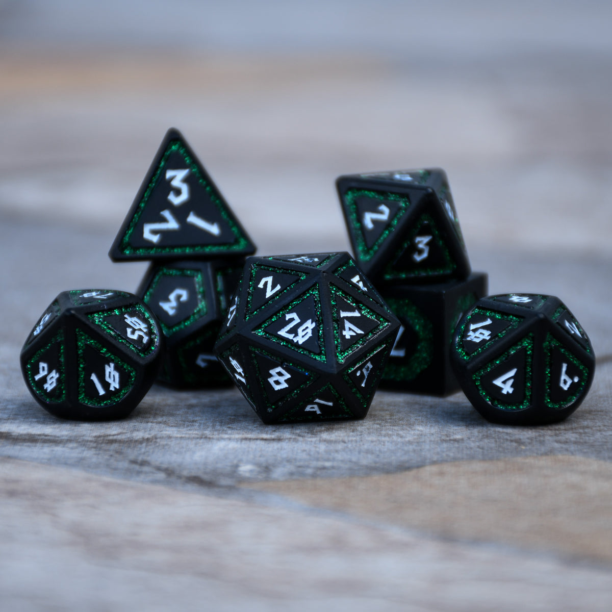 a set of black metal dnd dice with white numbering and deep green glitter borders on each face