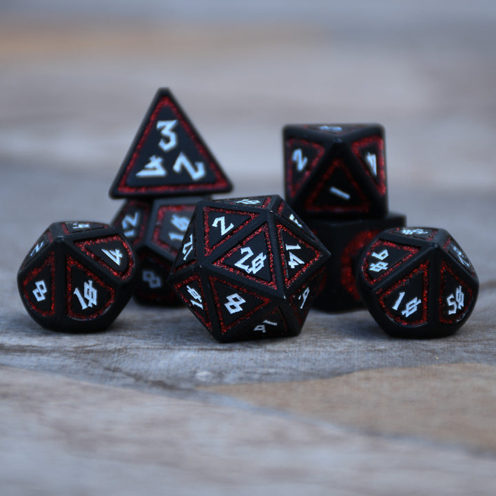 a set of black dnd metal dice with white numbering and red glitter border on each face on a light background