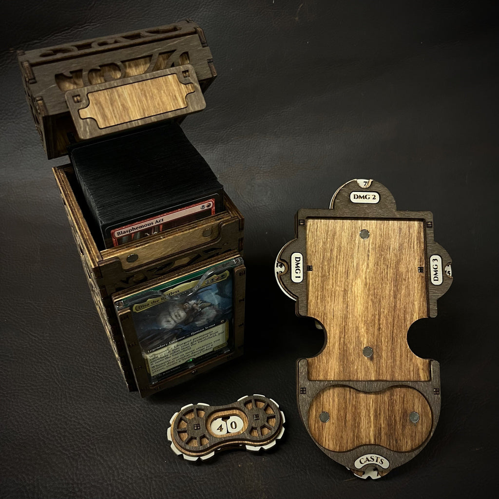 A wooden deck box with intricate cut-out patterns, featuring a purple interior, accompanied by a command plate and game tokens.