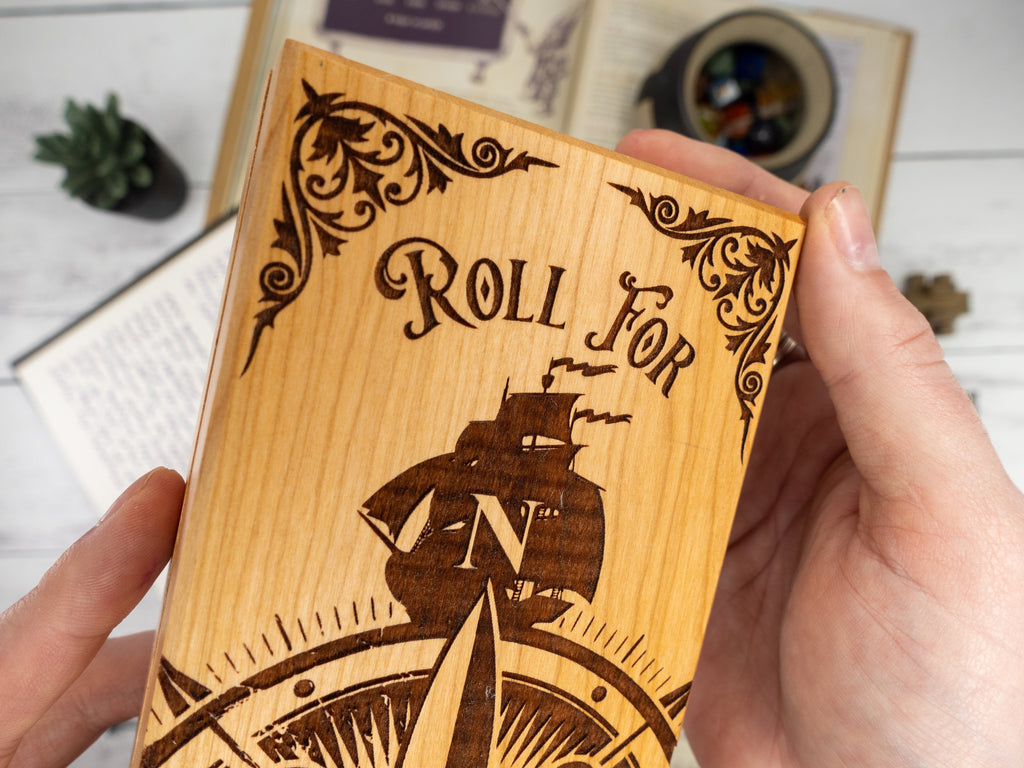 Wooden dice tray with 'Roll For' text and ship design, held by a hand.