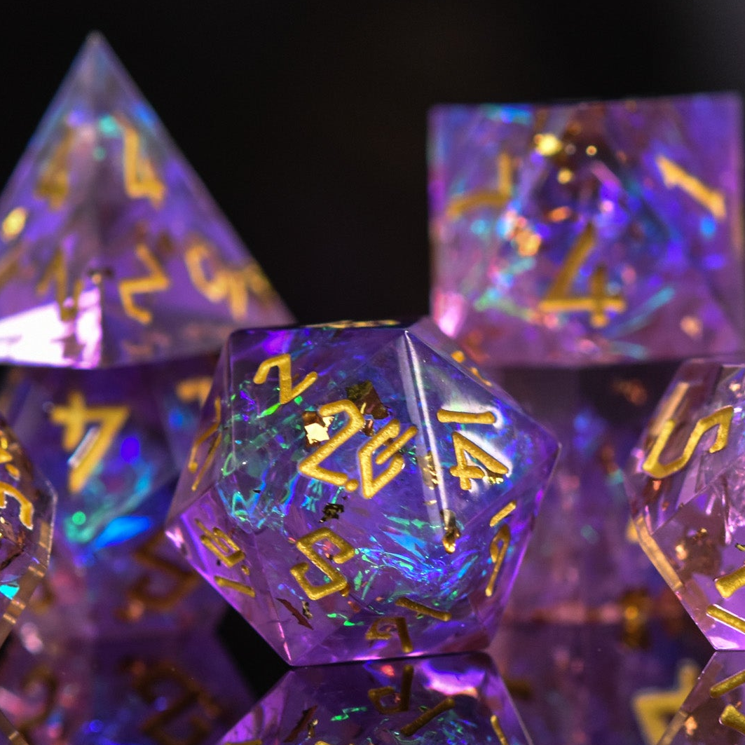 A set of sharp-edged, purple iridescent resin dice with engraved gold numbers, displaying a reflective surface.