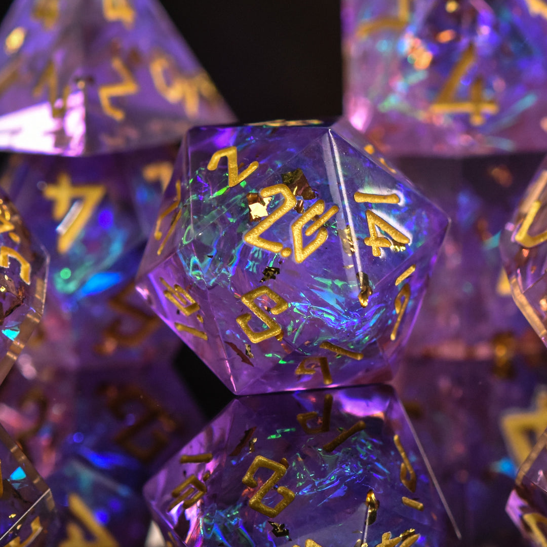 A set of sharp-edged, purple iridescent resin dice with engraved gold numbers, displaying a reflective surface.