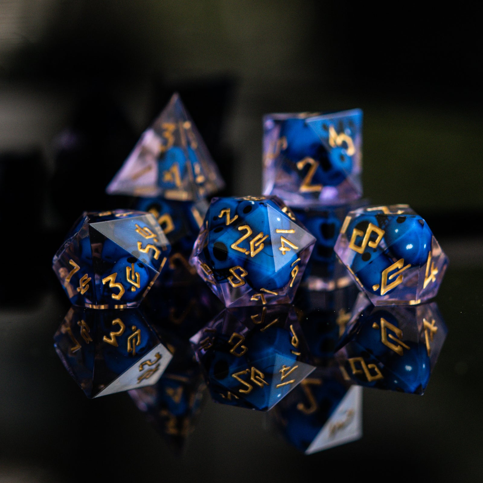 A set of sharp-edged resin dice in blue and lavender with engraved numbers, with blue skulls inside including various shapes such as a d4, d6, d8, d10, d12, and d20.