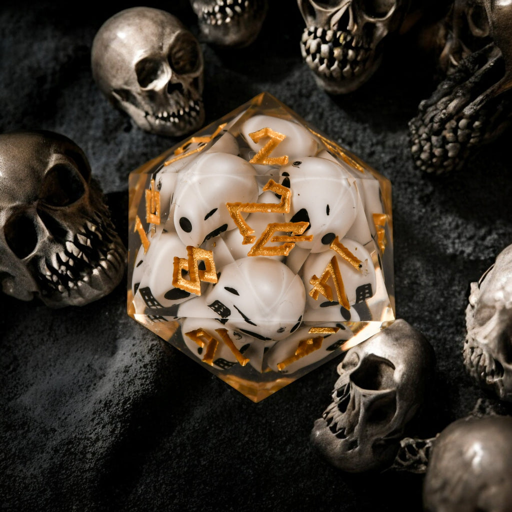 A clear resin dice filled with skulls with gold numbers, surrounded by small decorative skulls.