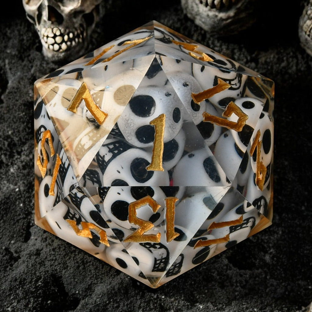 A clear resin dice filled with skulls with gold numbers, surrounded by small decorative skulls.