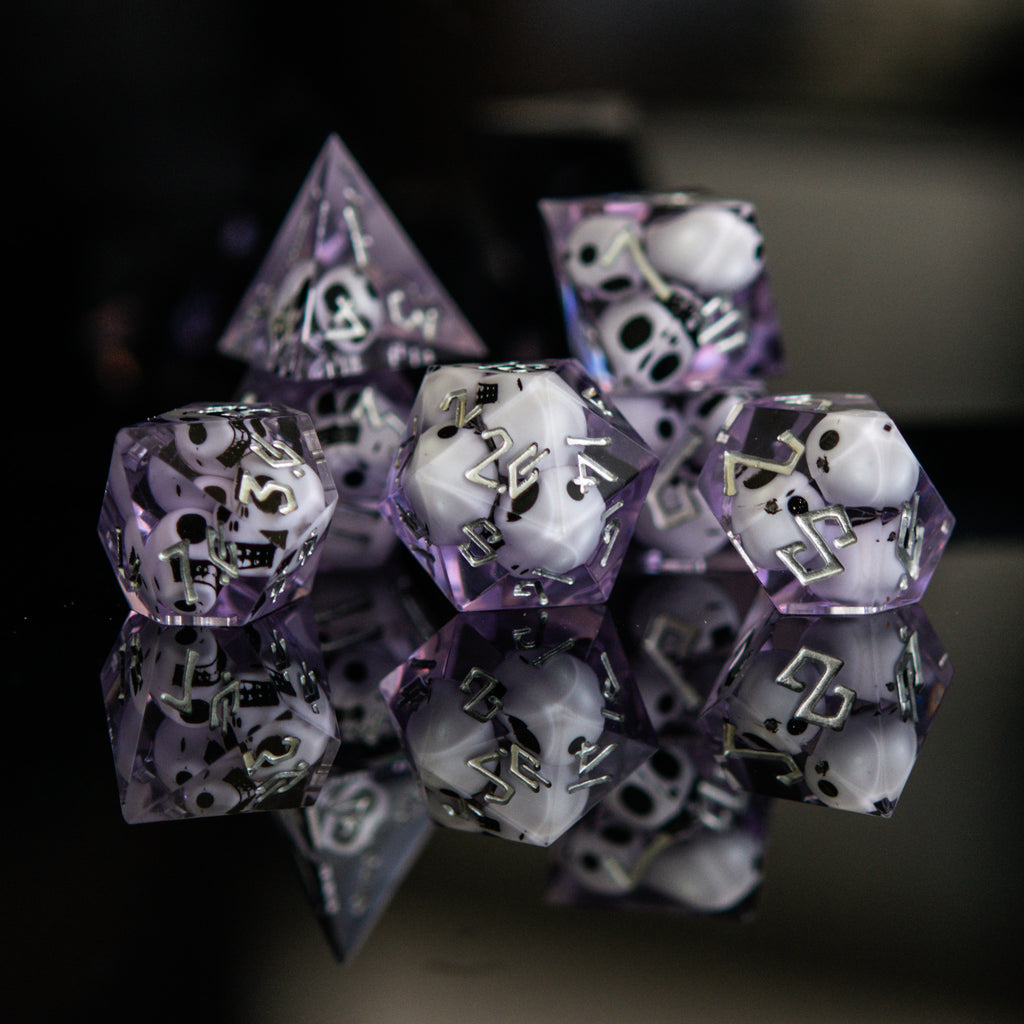 A set of sharp-edged resin dice in lavender with engraved numbers, with white skulls inside including various shapes such as a d4, d6, d8, d10, d12, and d20 for tabletop and board games