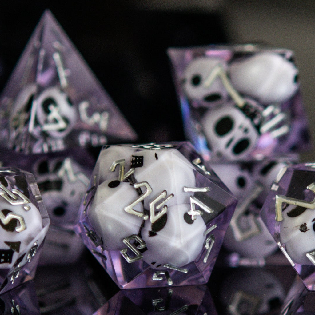 A set of sharp-edged resin dice in lavender with engraved numbers, with white skulls inside including various shapes such as a d4, d6, d8, d10, d12, and d20 for tabletop and board games