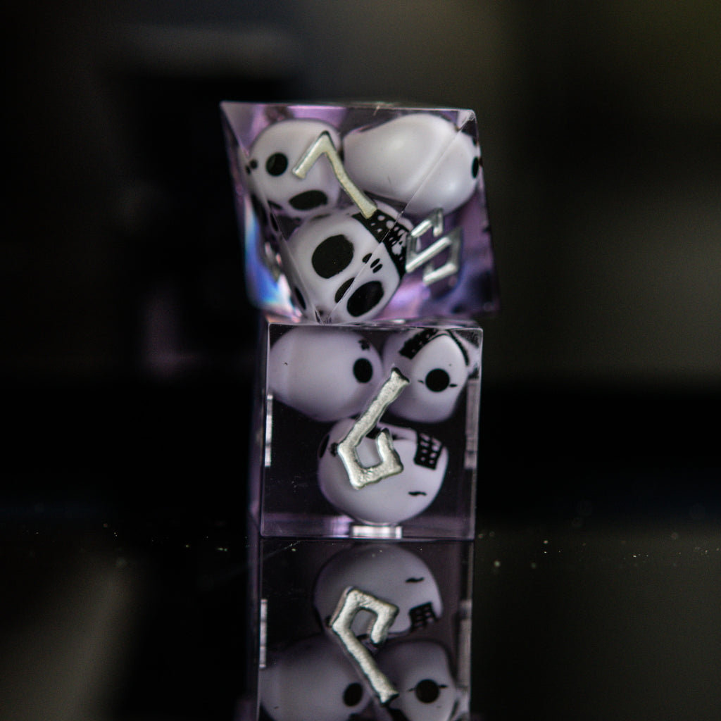 A set of sharp-edged resin dice in lavender with engraved numbers, with white skulls inside including various shapes such as a d4, d6, d8, d10, d12, and d20 for tabletop and board games