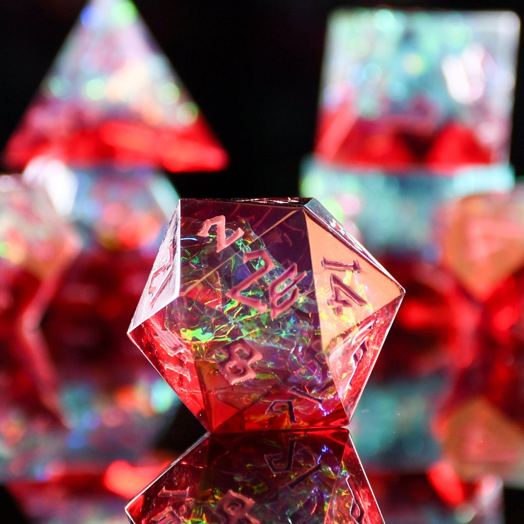 A set of sharp-edged, multicolored resin dice with hand-painted numbers, reflecting on a surface with a colorful backdrop.