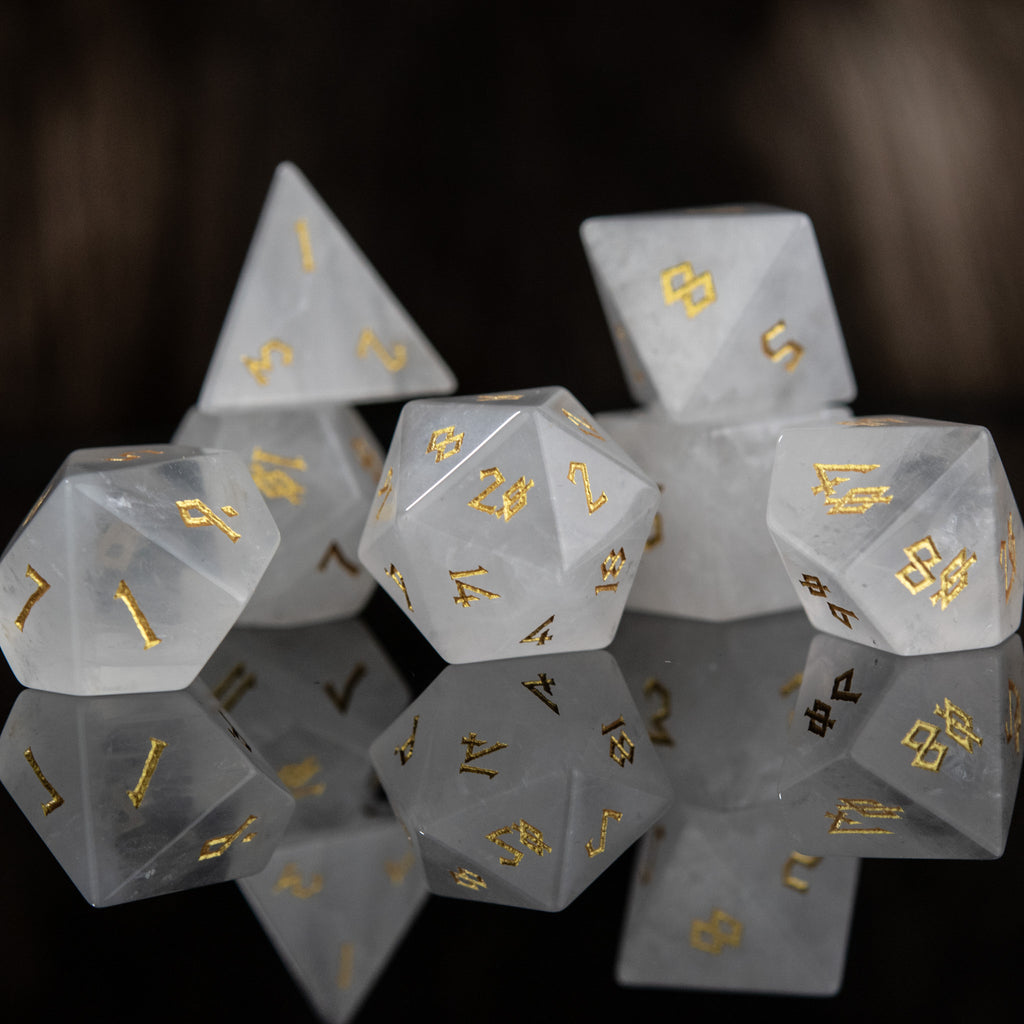 A collection of white crystal quartz stone dice with engraved numbers, displayed on a reflective surface.