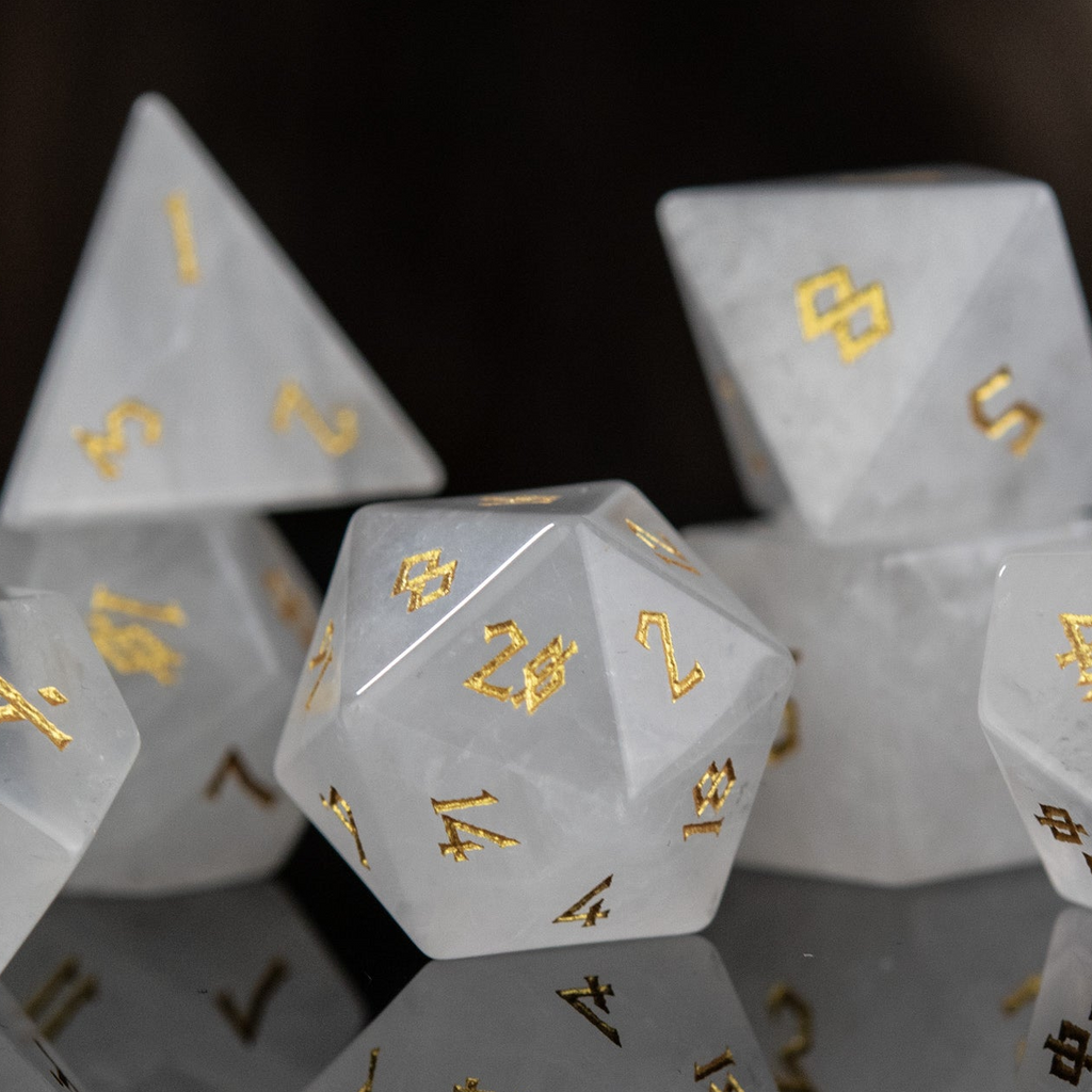 A collection of white crystal quartz stone dice with engraved numbers, displayed on a reflective surface.