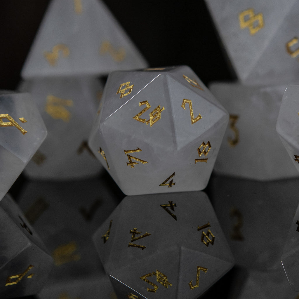 A collection of white crystal quartz stone dice with engraved numbers, displayed on a reflective surface.