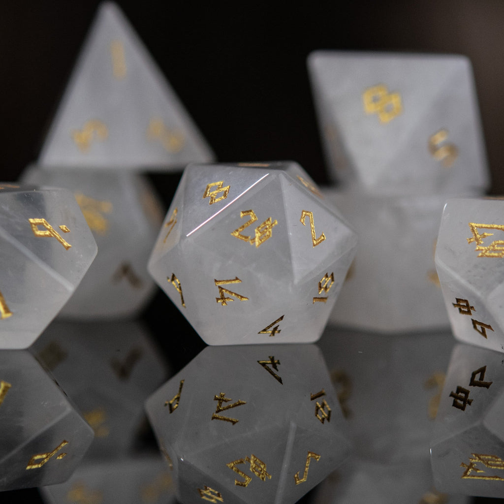 A collection of white crystal quartz stone dice with engraved numbers, displayed on a reflective surface.