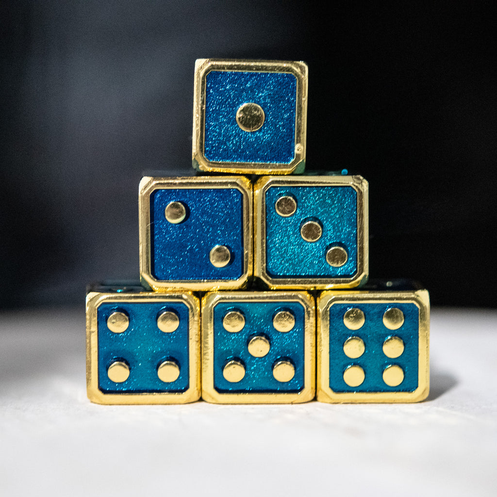 A stack of six metal d6 dice with aqua blue and gold colors, embossed with pips 