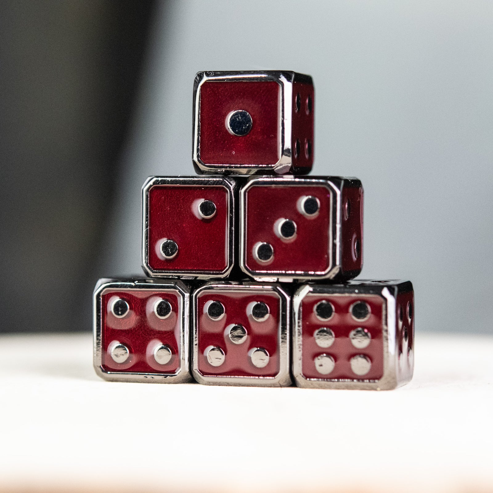 A stack of six red and black metal d6 dice with embossed numbers, representing a complete set.