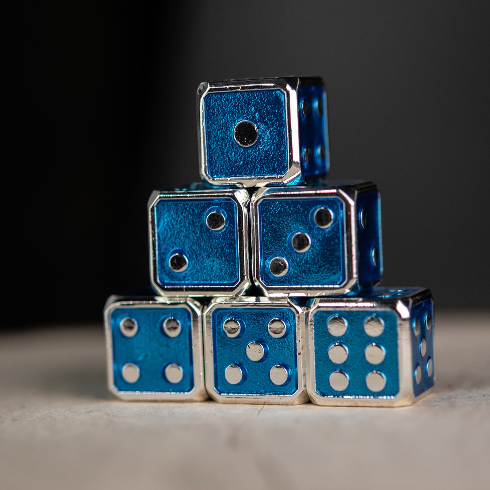 A stack of six blue metal dice with embossed silver pips