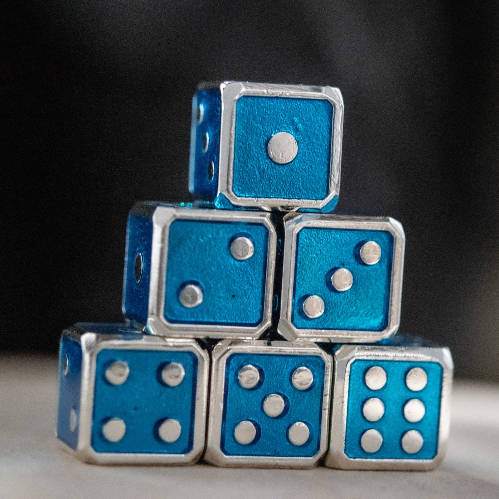 A stack of six blue metal dice with embossed silver pips