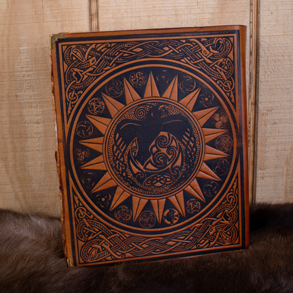 The back of a tan leather spell book journal featuring a raven within the sun