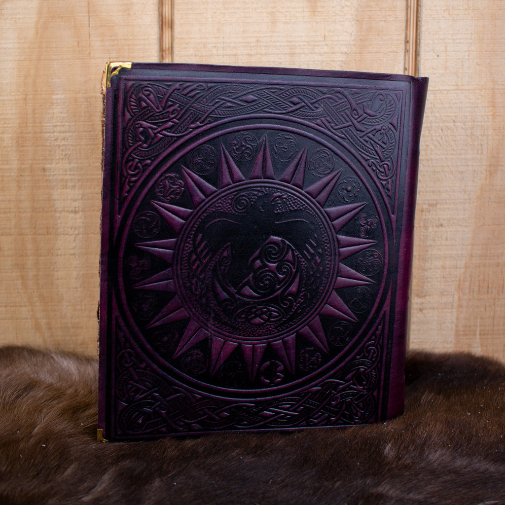 The back of a purple leather spell book journal featuring ravens and a sun
