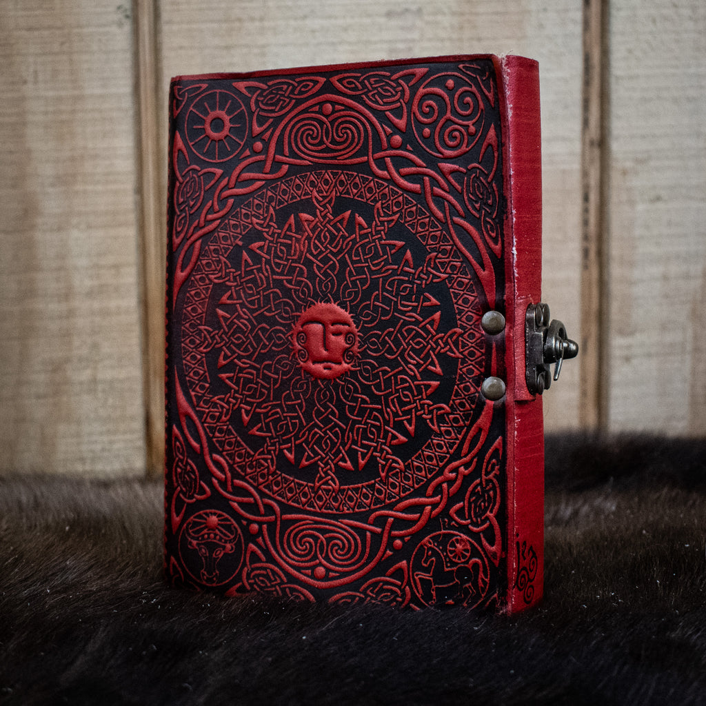 A red leather journal featuring a Celtic sun and moon
