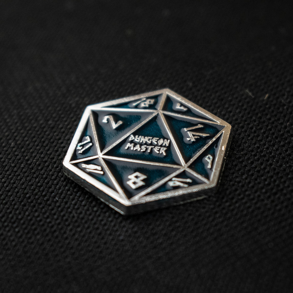 An aqua D20 pin with silver numbers in a Nordic font and "Dungeon Master" in the middle