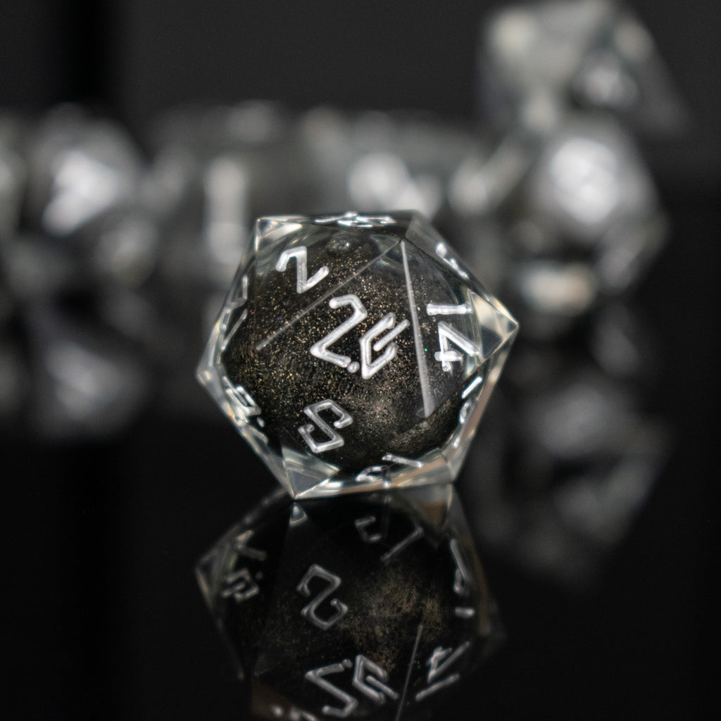 Black liquid and glitter inside of clear sharp resin dice with white numbers in a Nordic font