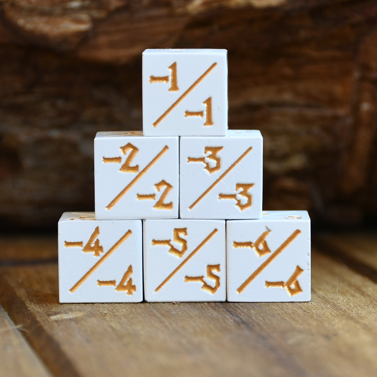 A set of white -1/-1 counter dice with numbers in orange, arranged in a pyramid shape on a wooden surface.