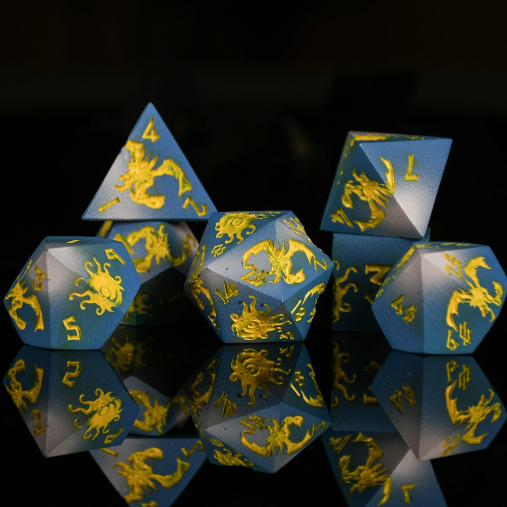 Set of blue polyhedral dice with yellow dragon designs on a reflective black surface.