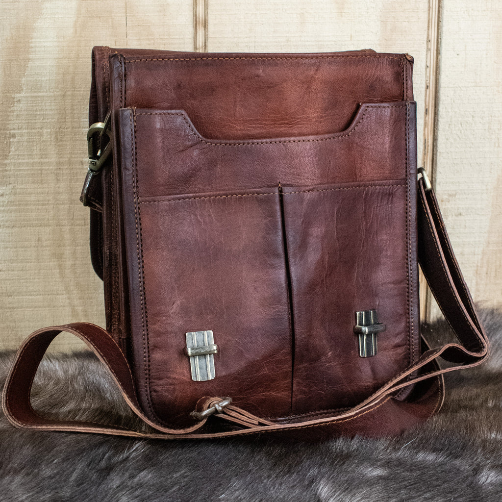 A brown full-grain leather bag with brass buckles, an adjustable strap, and pockets, displayed on a furry surface.