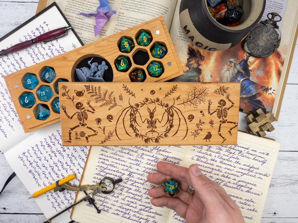 Wooden dice tray with engraved designs on a table with books and a cup.